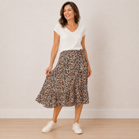 A woman modeling a white short-sleeve V-neck top and a brown leopard-print midi skirt with white sneakers, standing against a plain beige wall.