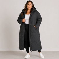 Woman wearing a long black coat against a plain background
