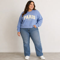 Woman wearing a blue sweatshirt with 'Paris France' text and blue jeans against a plain background